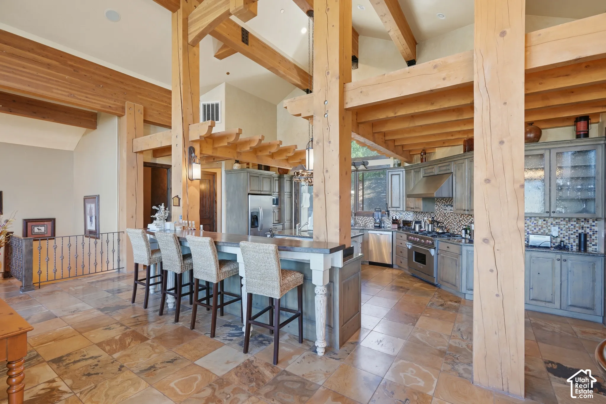 Exposed wood beams and columns, multi-toned tile flooring, kitchen with light gray cabinetry, stainless steel appliances, and a tiled backsplash