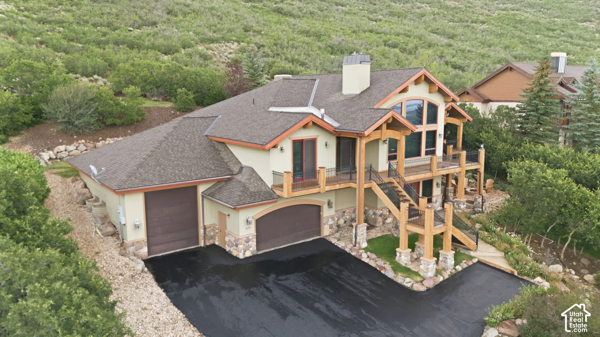 Multi-level residence featuring a prominent exterior staircase, dual attached garages, and a stone-clad foundation
