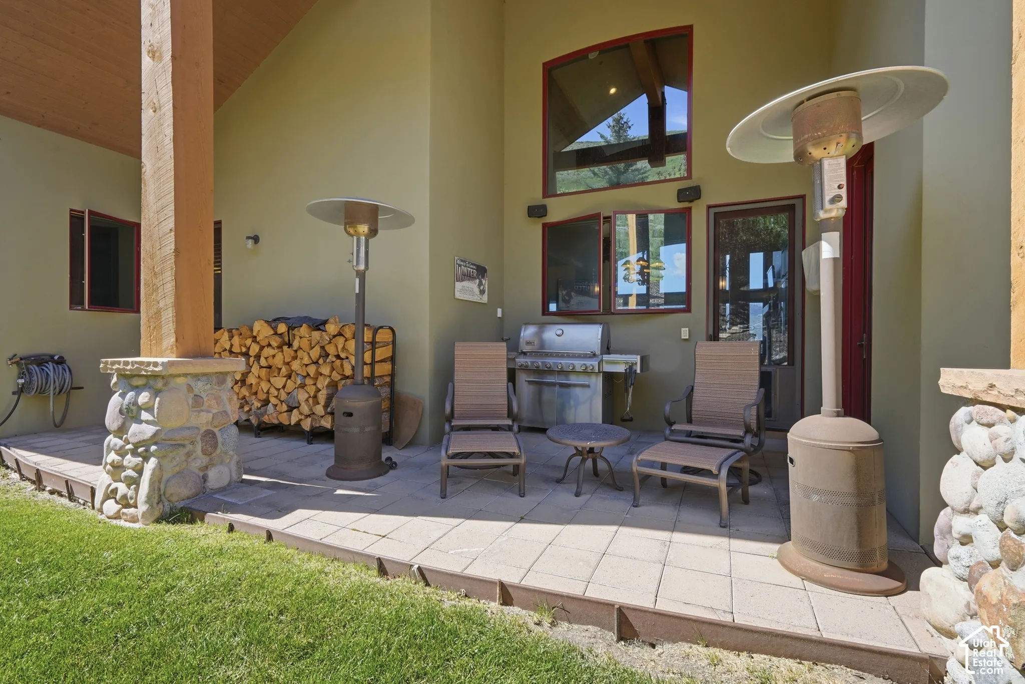 Expansive outdoor patio featuring a built-in grill, paver stone hardscaping, and stone-clad architectural columns
