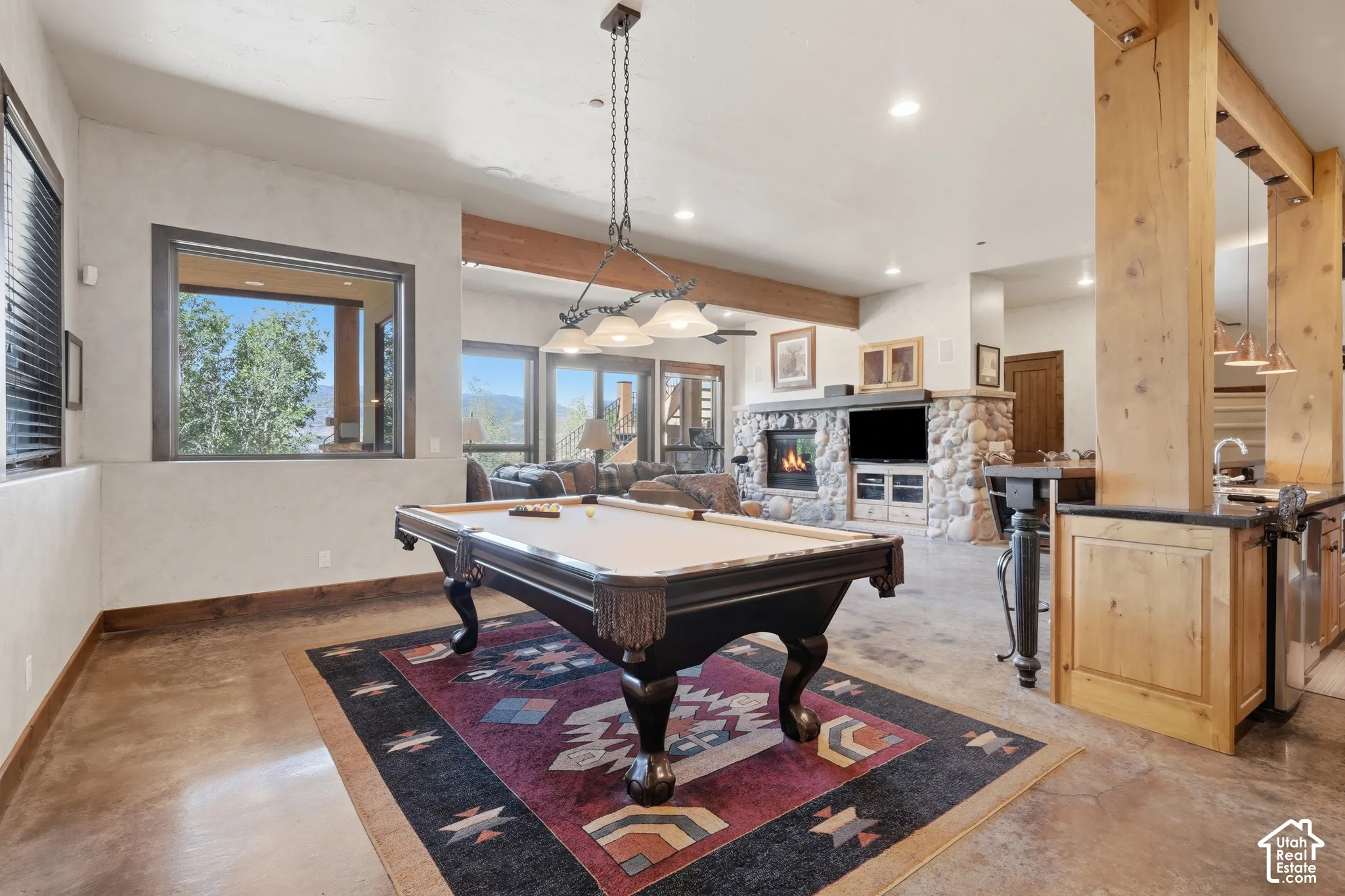 Spacious entertainment area with large picture window, exposed wood beams, and a stone-faced fireplace with built-in media storage