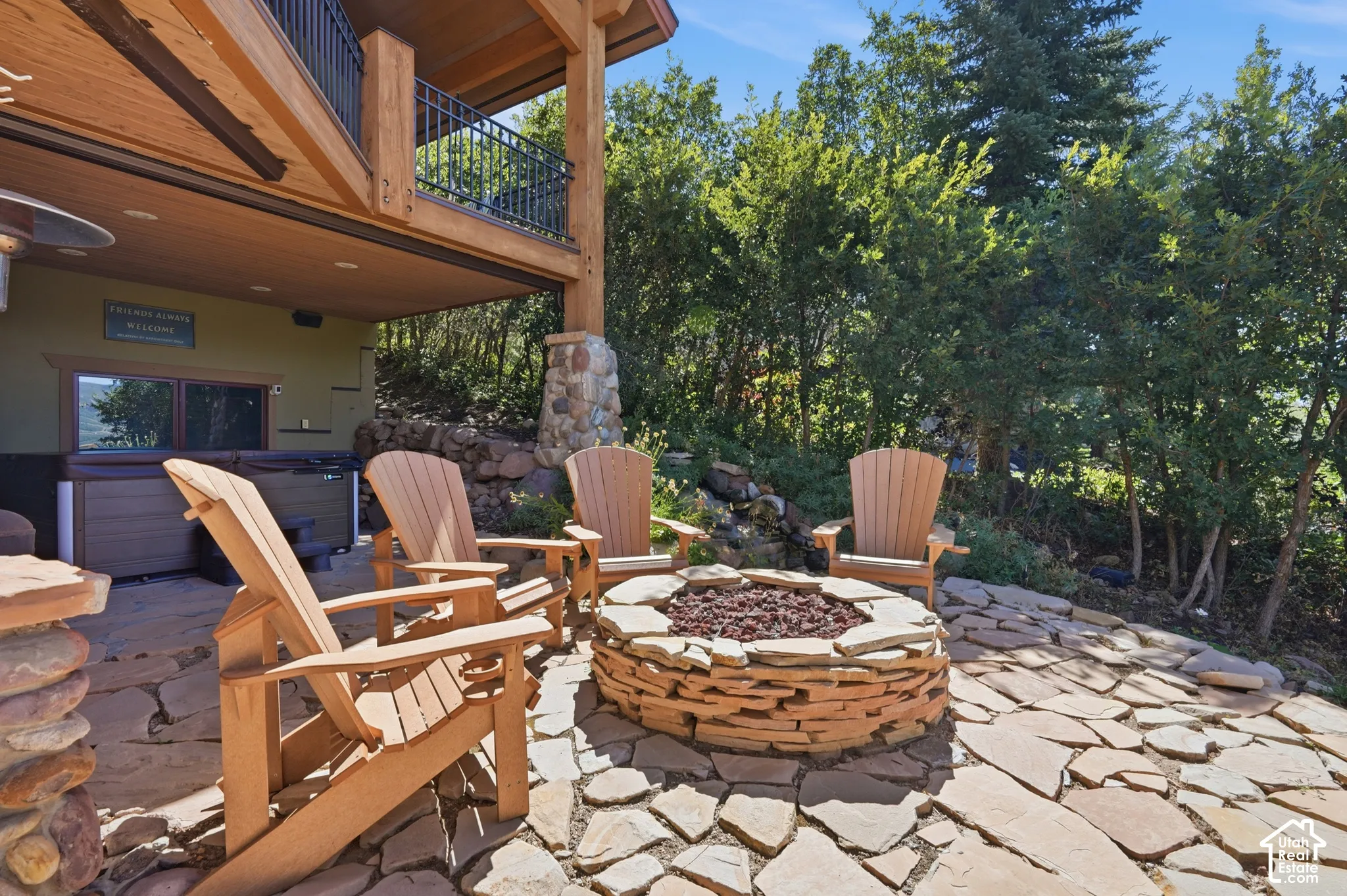 Expansive flagstone patio featuring a built-in fire pit, lush surrounding foliage, and a hot tub