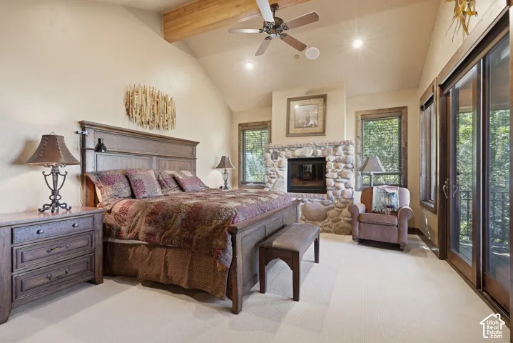 Vaulted ceiling with exposed wood beams, stone-clad fireplace, ceiling fan, and large glass sliding doors