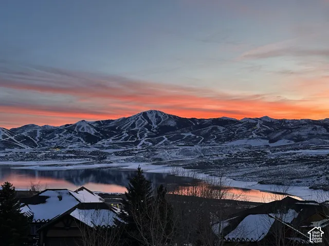 Snow-capped mountain range with visible ski slopes, large body of water, and residential structures with snow-covered roofs
