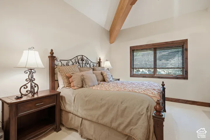 Vaulted ceiling with exposed wood beam, wood-trimmed window, and carpeted flooring