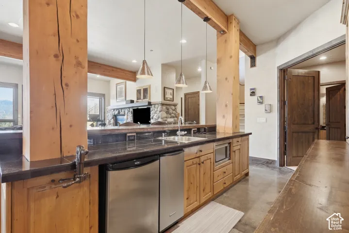 Stone fireplace with hearth, wood-finish beams, wood-finish cabinetry, stainless steel under-counter refrigerator, and stainless steel microwave