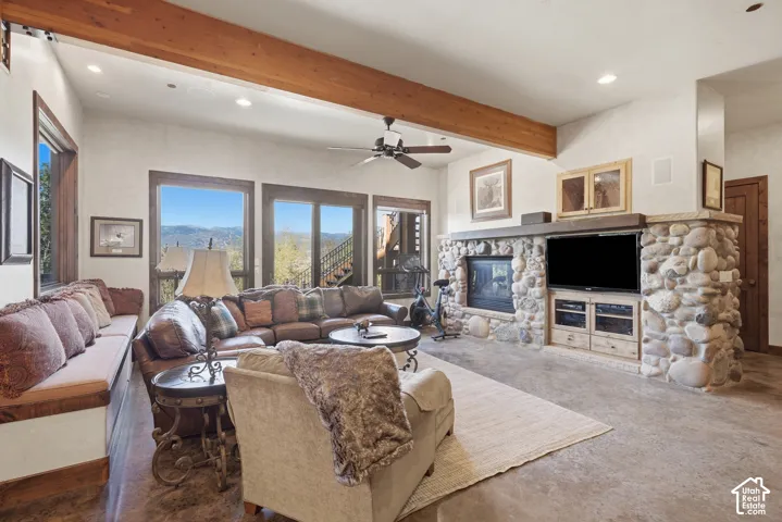 Exposed wooden beam, stone fireplace with hearth, wood-frame windows, built-in window seating, and a ceiling fan
