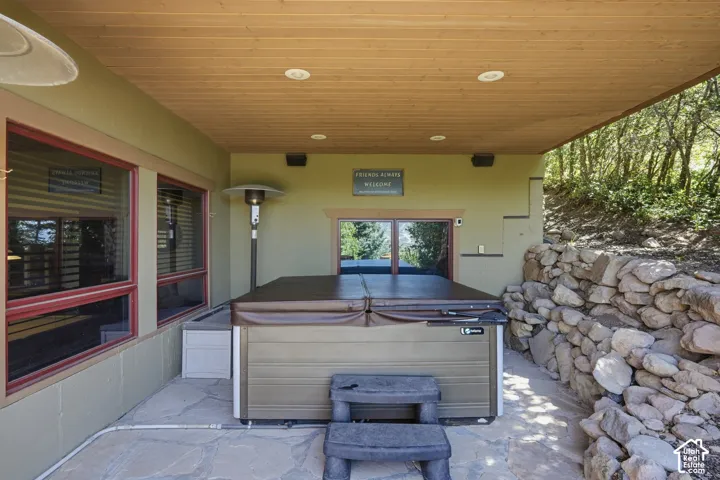 Covered patio featuring a hot tub, stone retaining wall, and wood-finish ceiling with recessed lighting