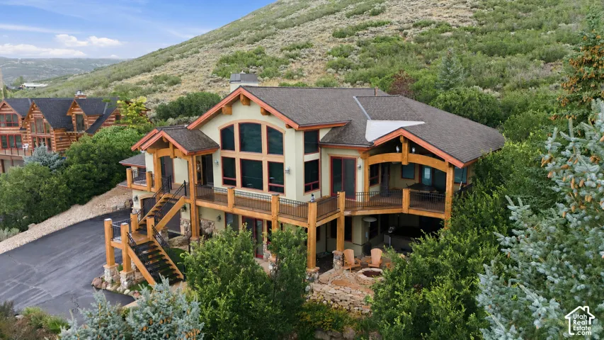 Multi-level exterior with extensive decking, a prominent stone chimney, arched window details, and a lower-level fire pit area