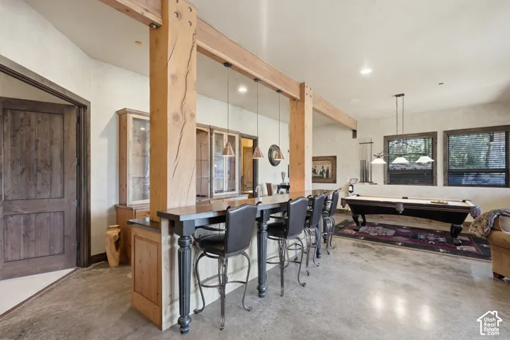 Exposed timber beams and columns with a built-in bar featuring a dark countertop, concrete flooring, and recessed lighting