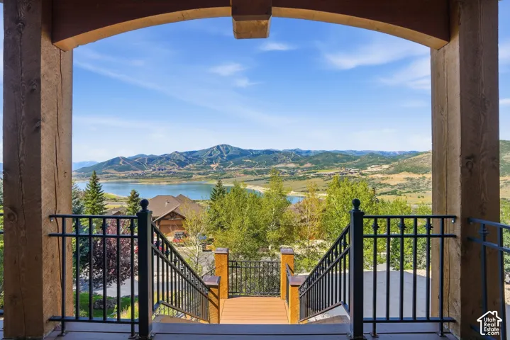 Arched wooden beam entryway with a spacious outdoor deck, wrought iron railings, and extensive water and mountain scenery