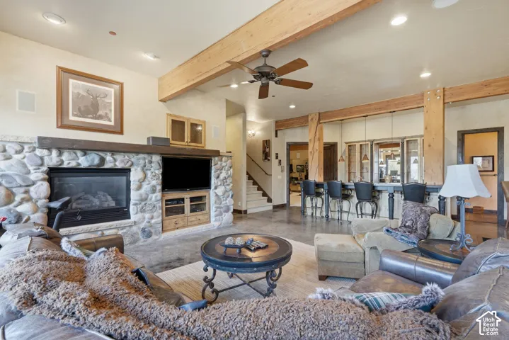 Stone-clad fireplace with a wood mantel, exposed wood beams, ceiling fan, and built-in bar with pendant lighting