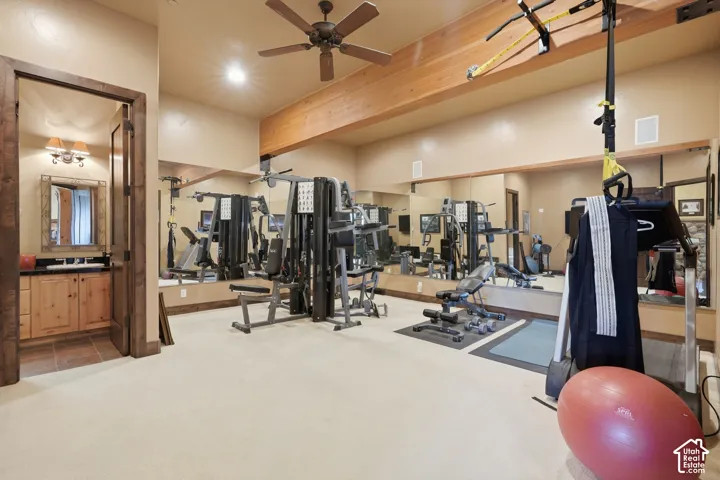 Dedicated home gym space featuring a ceiling fan, exposed wood beam, and mirrored wall