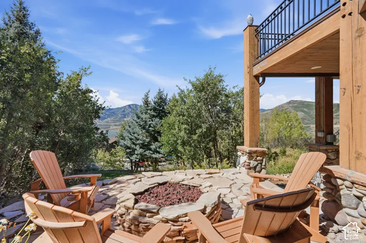 Outdoor stone patio featuring a built-in fire pit, stone retaining walls, and a wood-beamed overhead structure with a balcony above