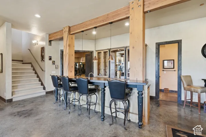 Polished concrete flooring, exposed wood beams, built-in bar with pendant lighting, and a staircase with a carpet runner