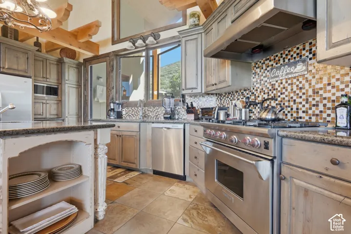 Full kitchen featuring distressed wood cabinetry, stainless steel appliances, a multi-tone tile backsplash, and a central island with an integrated display shelf