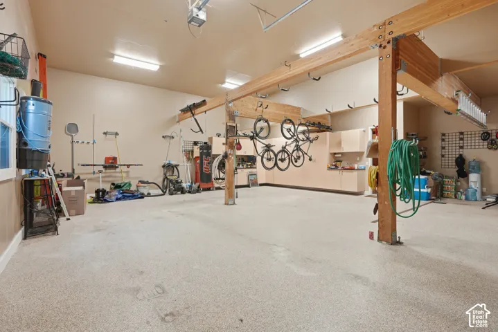 Spacious garage with exposed wood beam construction, integrated cabinetry, durable speckled flooring, and mounted ceiling lighting