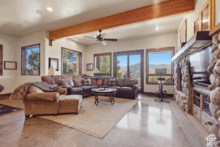 Exposed wood beam ceiling, expansive windows, floor-to-ceiling stone fireplace, recessed lighting, and concrete flooring