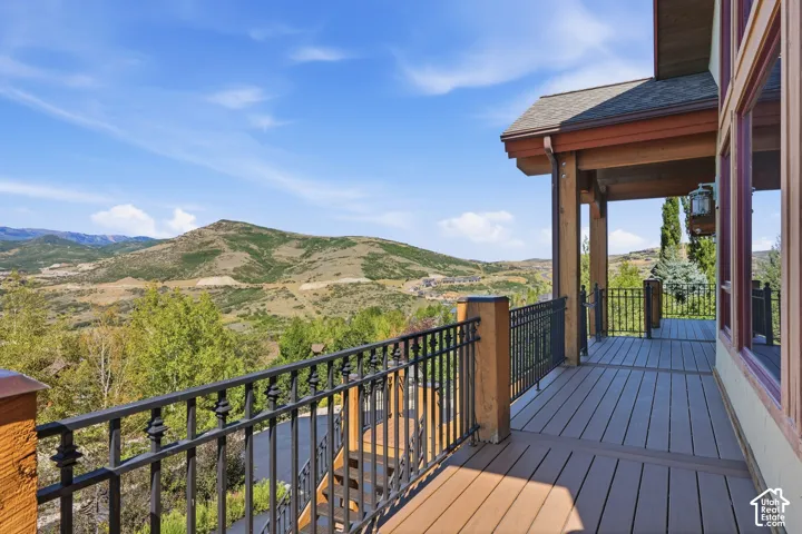 Expansive outdoor deck with mountain scenery, dark wood-finish decking, black wrought iron railing, and a covered porch area with exposed wood beams