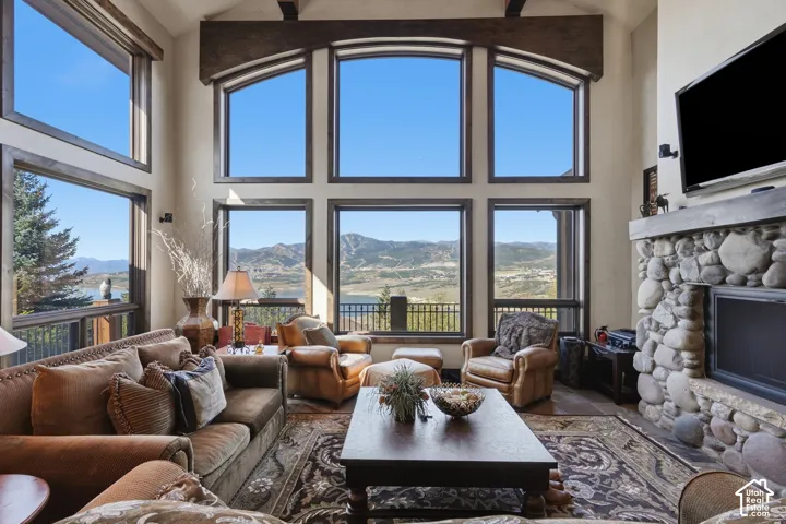 Two-story window wall, exposed wood beam accents, stone-faced fireplace, mountain and lake scenery, and large format floor tiles