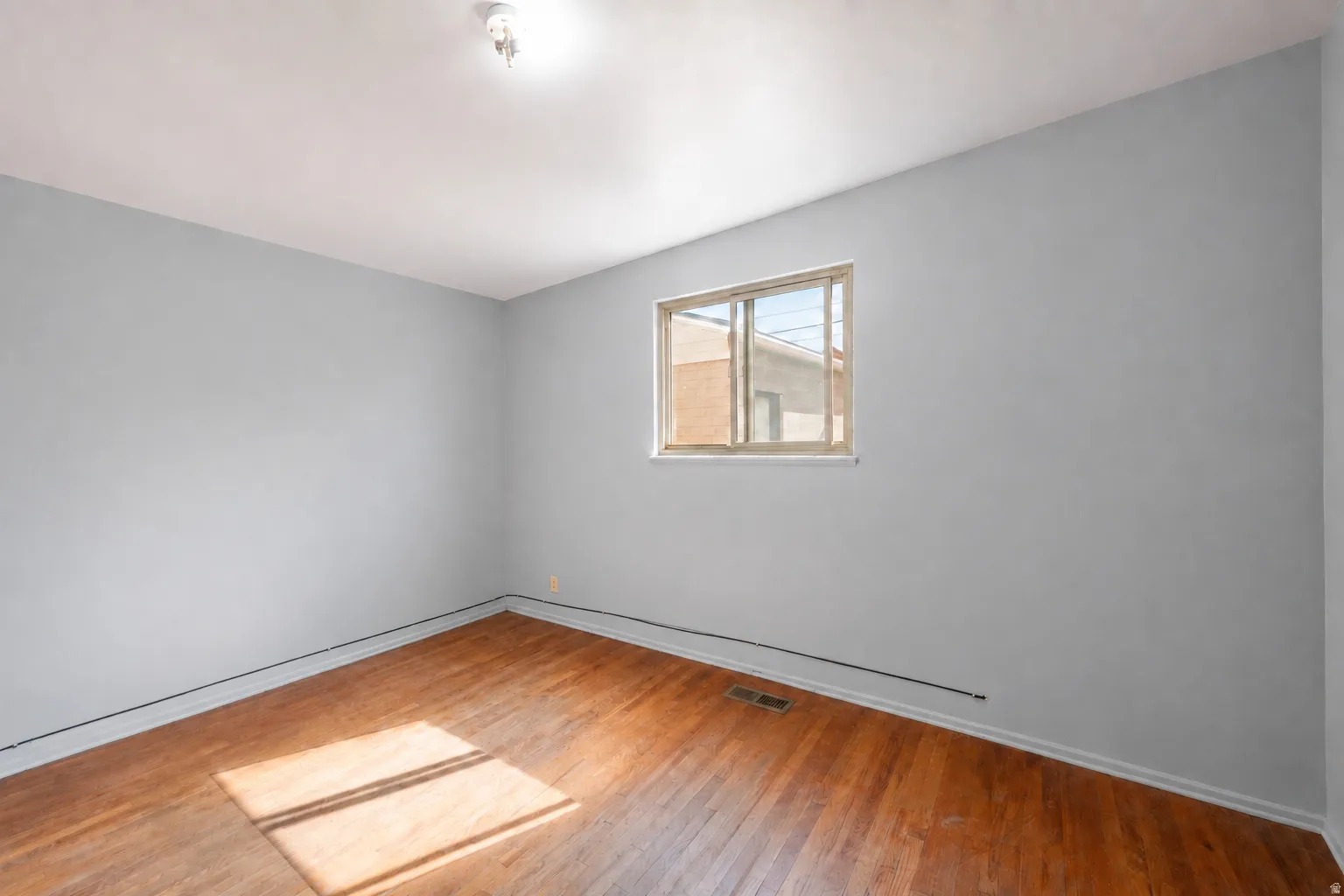 Hardwood flooring, light gray wall finish, window with natural light, and ceiling-mounted light fixture