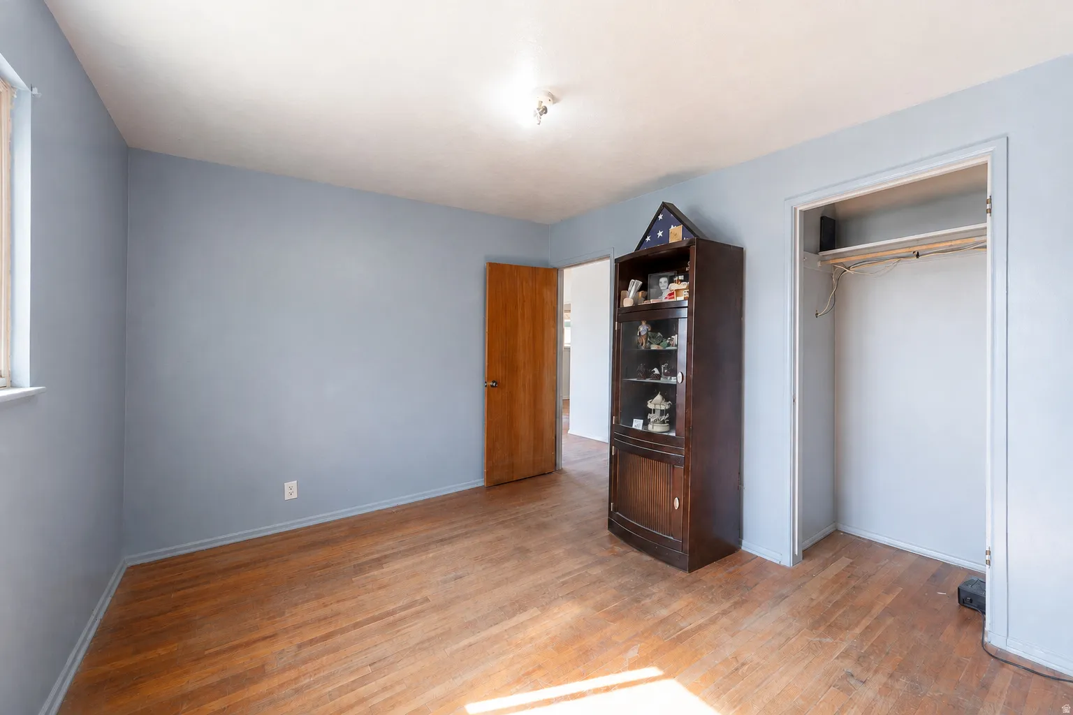 Hardwood flooring, window with natural light, closet with shelving, wood-finish door, and overhead lighting