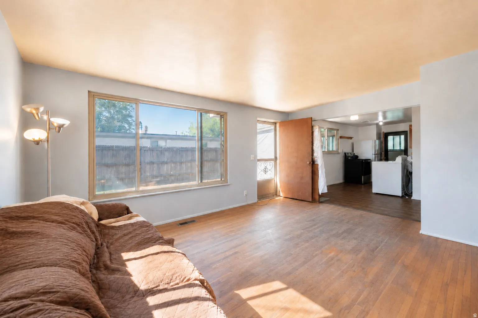 Light-filled living area featuring wood-finish flooring, a large picture window, and an open doorway to the kitchen