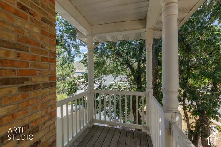 Exterior balcony with wood-finish flooring, white spindle railing, and decorative support columns