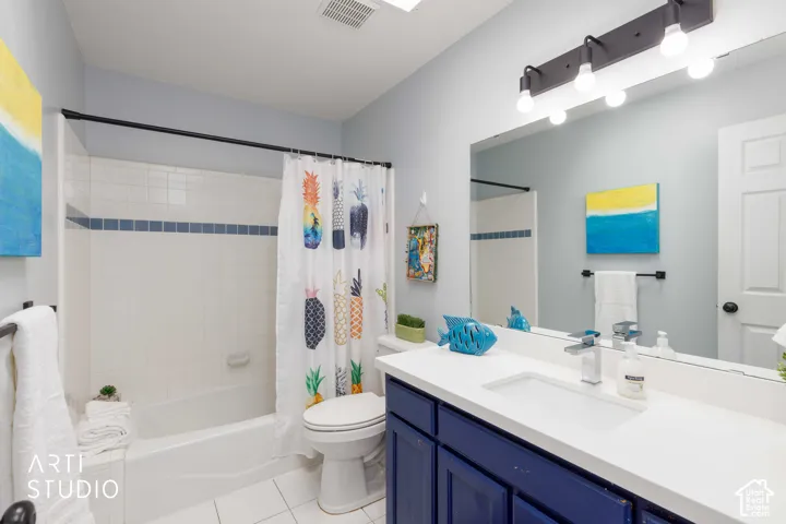 White tile flooring, white tile bath surround with blue accent band, white vanity countertop, undermount sink, and a dark blue vanity cabinet