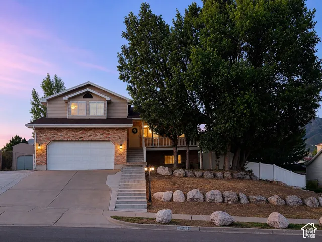 East Layton 4-bedroom home at twilight with brick and siding exterior with a two-car garage, concrete driveway, RV pad and a welcoming front porch with white railing