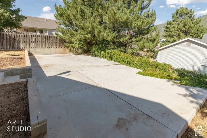 Expansive concrete patio with block retaining walls, surrounded by mature trees and a wooden fence