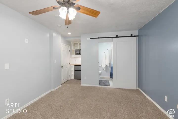 Mother-in-law suite with private bathroom and mini kitchenette with built-in microwave, ceiling fan, carpet flooring, and barn door entry to bathroom.