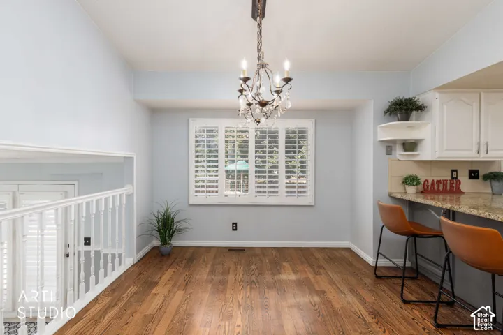 Hardwood flooring, white window shutters, ornate chandelier, white railings, and white kitchen cabinetry