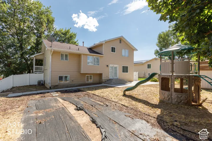 Rear exterior featuring tan siding, a ground-level patio, a white privacy fence, and mature trees