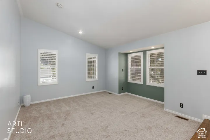 Vaulted ceiling with recessed lighting, light-toned carpet flooring, multiple windows with white shutters, and a contrasting accent wall