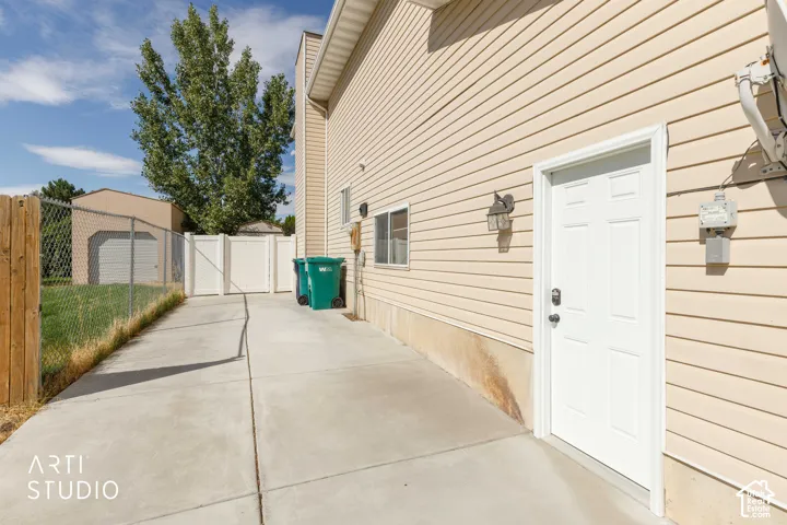 Side entrance door with exterior wall sconce, concrete walkway, and vinyl privacy fence