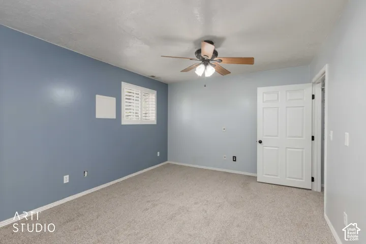 Light-colored carpeting, a ceiling fan with integrated lighting, window with white plantation shutters, and a paneled interior door with dark hardware