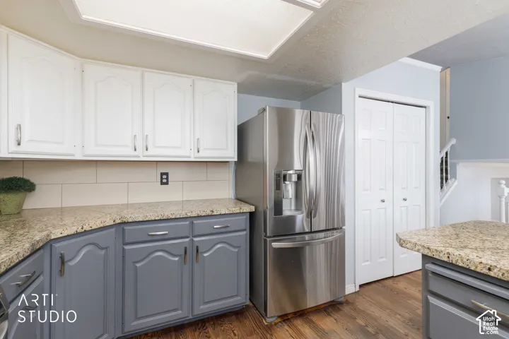 Two-tone cabinetry with upper white cabinets and lower gray cabinets, light-toned countertops, tile backsplash, and wood-finish flooring