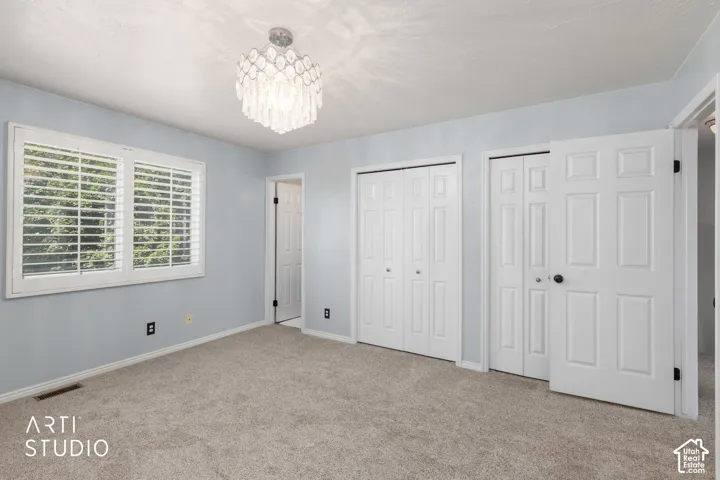 Primary bedroom with plush carpet flooring, a decorative overhead light fixture, white window shutters, and two sets of bi-fold closet doors