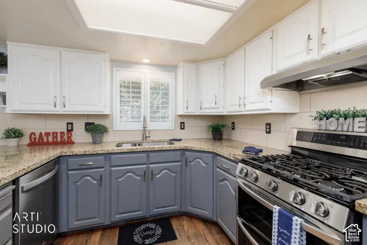 Kitchen featuring wood-finish flooring, two-tone cabinetry, stainless steel appliances, granite-style countertops, and a tile backsplash