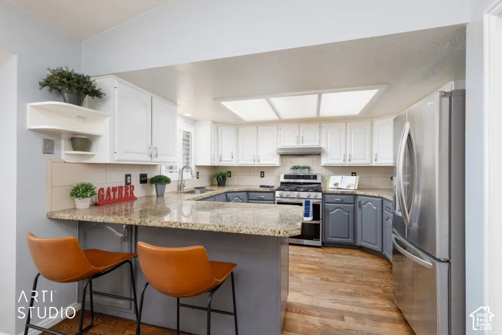 Kitchen featuring wood-finish flooring, two-tone cabinetry, stainless steel appliances, a breakfast bar, and recessed lighting