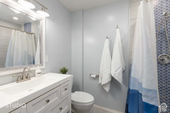 Vanity with integrated sink, brushed nickel faucet, mirror with light fixture, patterned blue tile shower surround, and light wood-finish flooring
