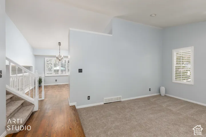 Wood-finish flooring, staircase with carpeted treads, white painted railings, and a window with white plantation shutters