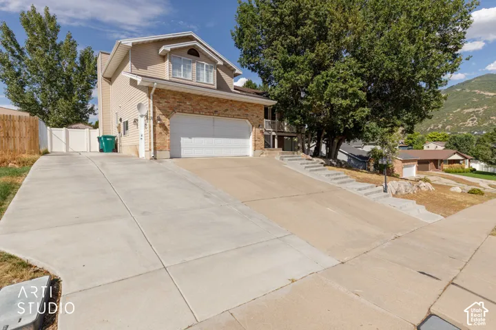 Split-level residence featuring a two-car garage, concrete driveway, and mature landscaping