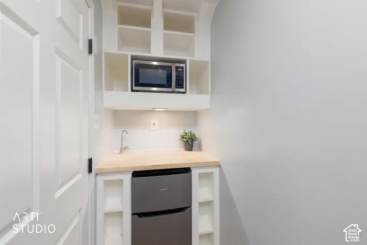 Built-in cabinetry with open shelving, integrated microwave, wood-finish countertop, under-cabinet lighting, and compact refrigerator