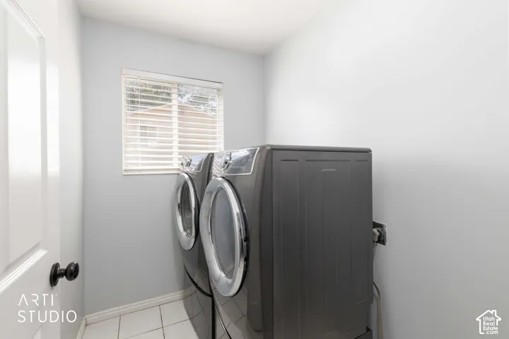 Laundry room with lots of natural light, tile flooring, a window with horizontal blinds, and a white interior door with a dark knob. Not shown: laundry chute
