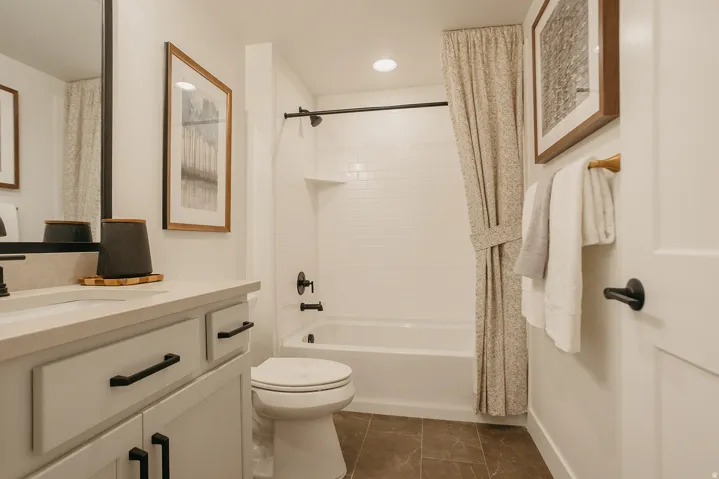 White subway tile shower surround with integrated shelf, black-finish plumbing fixtures, white vanity with stone-finish countertop, and dark rectangular floor tiles