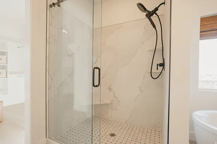 Glass-enclosed shower featuring large format wall tile, a built-in bench, and black hexagonal floor tiles