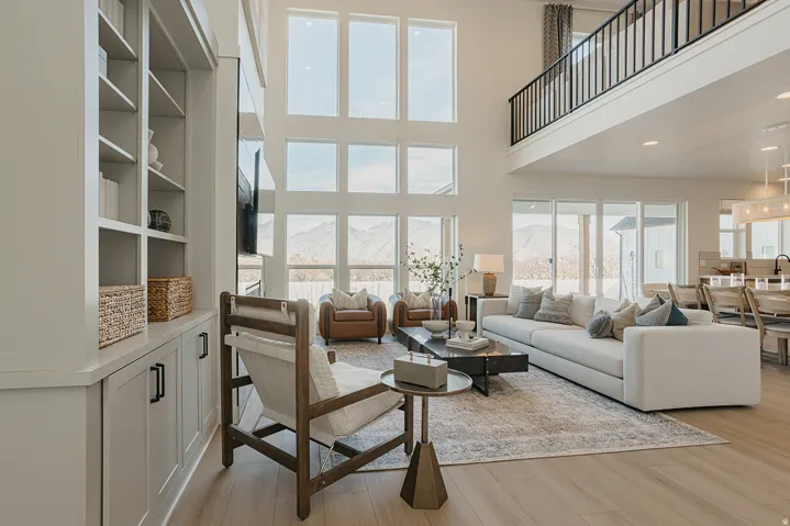 Two-story living area with expansive window walls, light wood-finish flooring, built-in shelving, and an upper-level balcony with iron railings