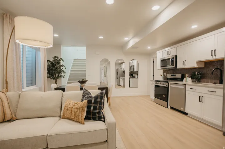 Open-concept living space featuring wood-finish flooring, recessed lighting, and a kitchen with white cabinetry, stainless steel appliances, and a dark tile backsplash