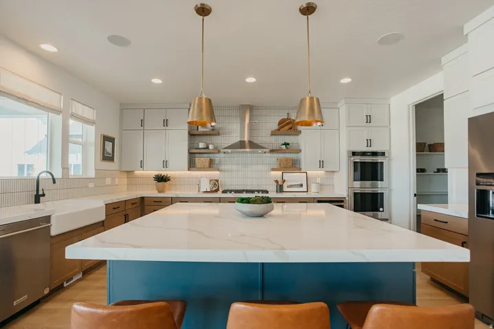 Kitchen featuring a spacious island with a light-toned countertop, brass pendant lighting, stainless steel double ovens, and a farmhouse sink